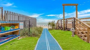 A pathway leading to a wooden structure with a signboard, a beach in the background, and a clear sky. - Retreat by the Sea (Myrtle Beach)