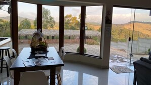 A dining area with a table set for two, large windows offering a view of a hilly landscape, and a chandelier above.