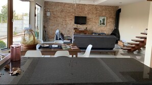 A modern living room with a brick wall, a flat-screen TV, a sofa, and a dining area with a table and chairs.