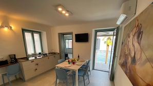 Une cuisine compacte avec un coin repas, un téléviseur fixé au mur et un balcon offrant une vue sur les palmiers.