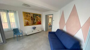 Un salon moderne avec un canapé bleu, une console blanche ornée d’un vase et un grand tableau abstrait accroché au mur.