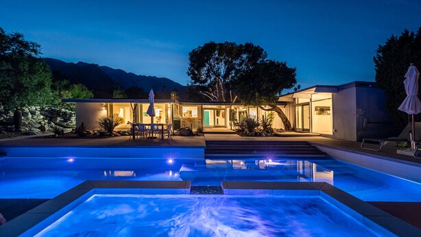 Una casa moderna amb piscina, zona d'estar a l'aire lliure i vistes a les muntanyes.