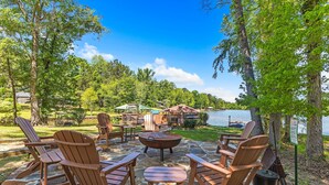 An outdoor seating area with Adirondack chairs, a fire pit, and a view of a lake.