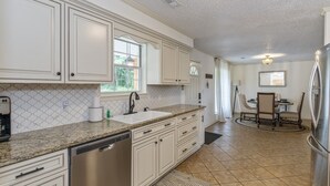 A kitchen with white cabinets, a granite countertop, a dishwasher, and a dining area with a table and chairs.