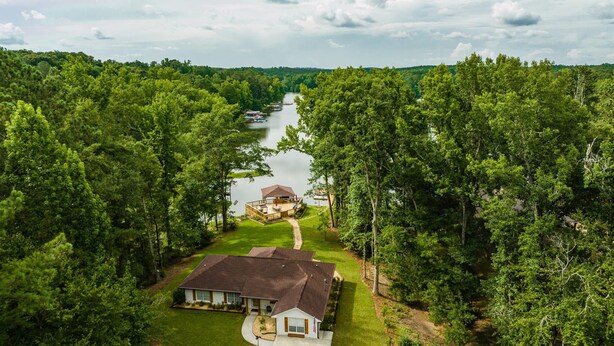 A house with a deck overlooking a lake, surrounded by dense forest.