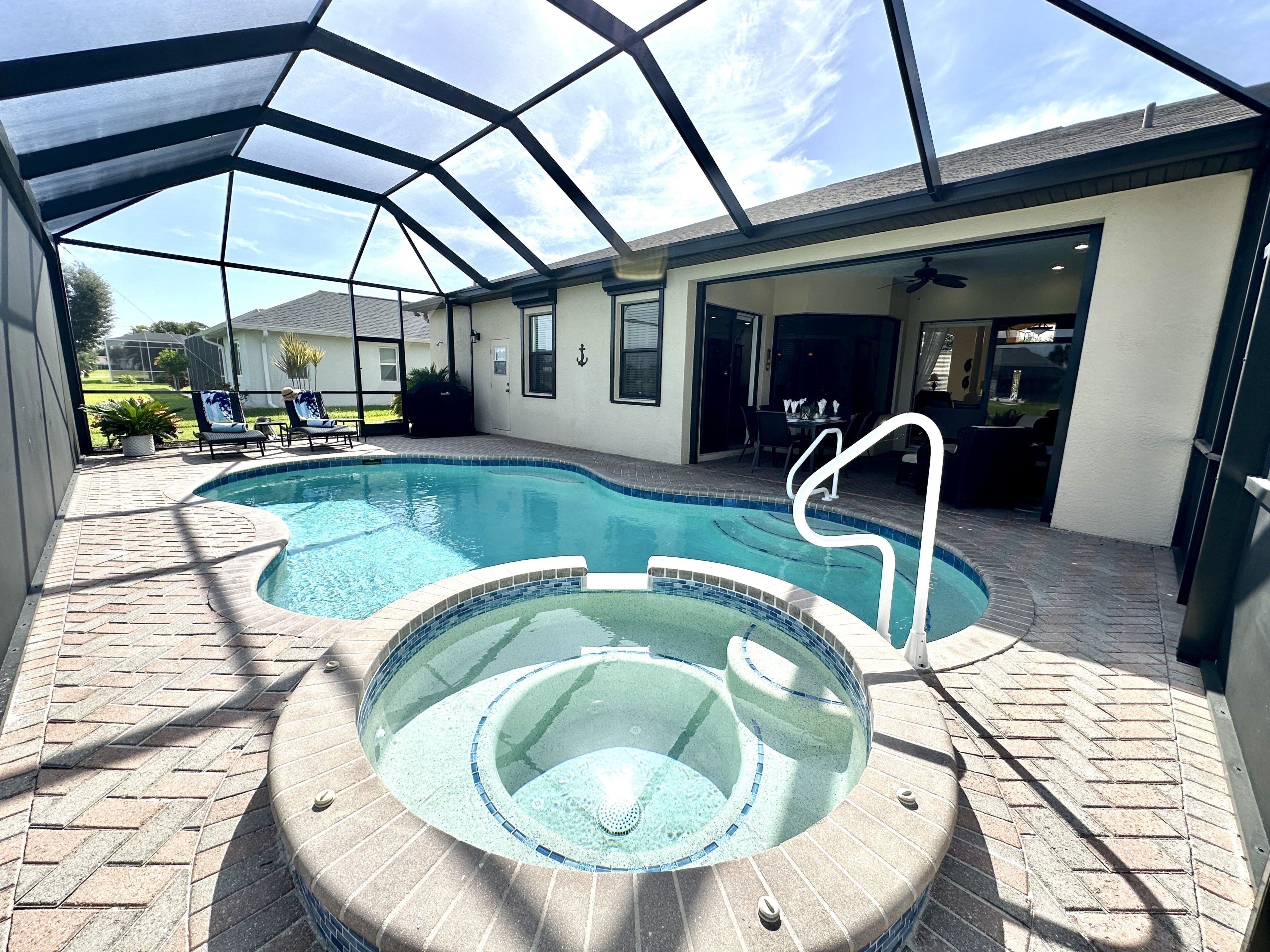 A covered swimming pool with a hot tub, lounge chairs, and a patio area.