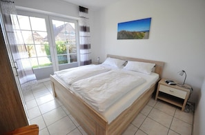 Un dormitorio con una cama grande, una mesita de noche con lámpara y una ventana con vistas a edificios y vegetación.