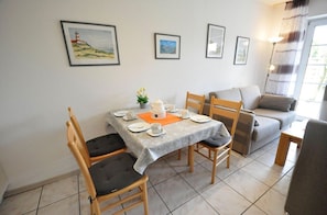 Un comedor con una mesa dispuesta para dos personas, sillas, un sofá y una lámpara.