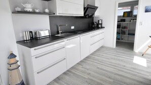A modern kitchen with white cabinetry, a black countertop, and stainless steel appliances. - meinStrandhaus - Holiday home "meinStrandhaus" (Neuharlingersiel)