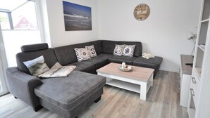 A modern living room with a grey sofa, a coffee table, and a clock on the wall. - meinStrandhaus - Holiday home "meinStrandhaus" (Neuharlingersiel)