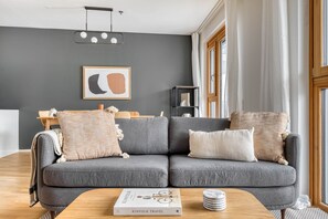 Uma sala de estar moderna com um sofá cinzento, uma mesa de centro de madeira e uma pintura abstrata emoldurada na parede.