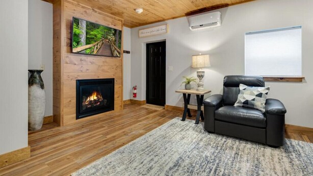 Una sala de estar acogedora con chimenea, un sillón de cuero cómodo, una mesita con lámpara y un cuadro de un sendero en el bosque en la pared.