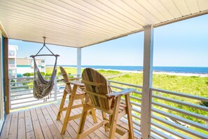 A wooden deck with a hammock, a rocking chair, and a view of the beach and ocean.