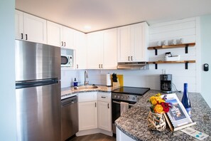 A modern kitchen with white cabinets, stainless steel appliances, a granite countertop, and a coffee maker.