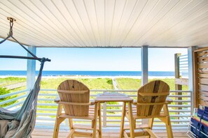 Een houten terras met twee stoelen en een tafel, met uitzicht op een strand.