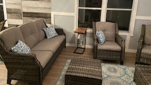 A living room with a brown sofa, two wicker chairs, a small table, and a patterned rug.