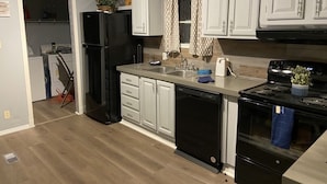 A modern kitchen with white cabinets, a black refrigerator, a dishwasher, a stove, and a sink.