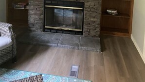 A living room with a stone fireplace, a mounted television, and a bookshelf.