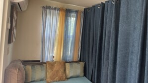 Quarto com sofá-cama, janela com cortinas e ar condicionado na parede.
