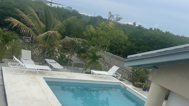 Piscina retangular com cadeiras de descanso brancas e um espaço com piso de azulejos.