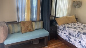 Quarto com cama, um banco e mesa de cabeceira.