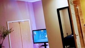 Habitación de hotel con televisión, espejo, puerta de madera y una silla amarilla.