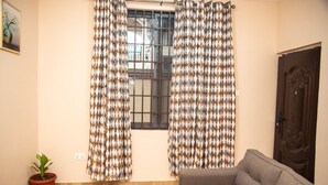 A room with a window, a sofa, a door, and a potted plant. - Captivating 1-Bed Apartment in Tema, com 25 (Tema, com 25)