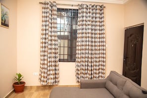 A room with a window, a sofa, a door, and a potted plant. - Captivating 1-Bed Apartment in Tema, com 25 (Tema, com 25)