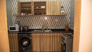 A compact kitchen with wooden cabinets, a built-in microwave, a washing machine, a sink, and a stove. - Captivating 1-Bed Apartment in Tema, com 25 (Tema, com 25)