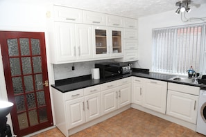 Compact kitchen with microwave, toaster, and sink, featuring a red-framed door and brown tile flooring.