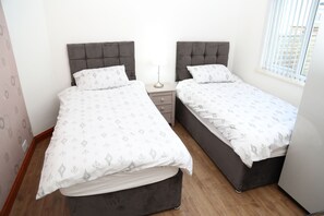 Two single beds with grey headboards and white bedding, each with a bedside table for personal items.