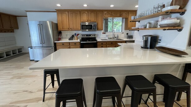 A modern kitchen with wooden cabinets, a large island with bar stools, stainless steel appliances, and built-in shelves. - Mid-Century Modern Gem next to Trails, Ski Resorts and Downtown Ogden (Ogden)
