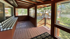 A covered porch with wooden flooring, a checkered bench, and large windows offering views of a backyard with a tree and a shed. - Mid-Century Modern Gem next to Trails, Ski Resorts and Downtown Ogden (Ogden)
