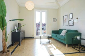 Una sala de estar con un sofá verde, una mesita redonda, una planta en maceta y un mueble negro.
