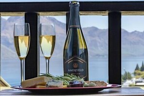 A bottle of Amisfield wine, two glasses of white wine, and a plate with cheese and vegetables on a table with a mountain view.