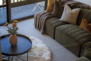 Un salon chaleureux avec un canapé, une petite table ronde ornée d’un vase de fleurs et un tapis moelleux.