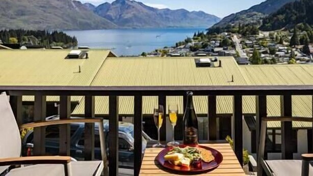 A dining area with a table set for two, overlooking a mountainous landscape and a body of water. - Mountain Vista 06, Magic Mountain Vista 06 (Queenstown)