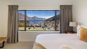 A hotel room with a large window, a bed, a bedside table, and a lamp. - Mountain Vista 06, Magic Mountain Vista 06 (Queenstown)