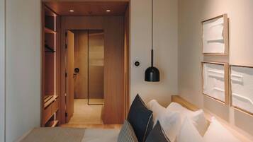 Habitación de hotel moderna con un armario de madera, cama con almohadas blancas y estampadas, una lámpara colgante negra y cuadros en la pared.