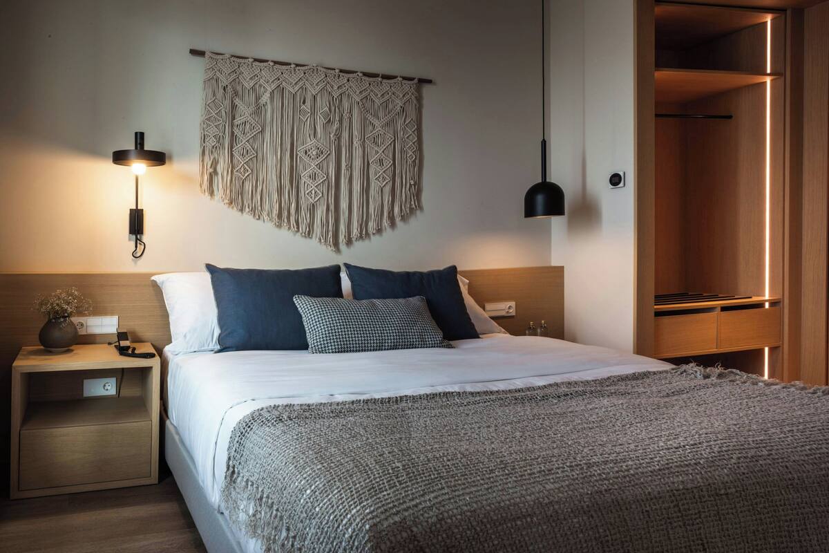 Un dormitorio ordenado con cama, mesitas de noche, un macramé colgado en la pared y un armario.