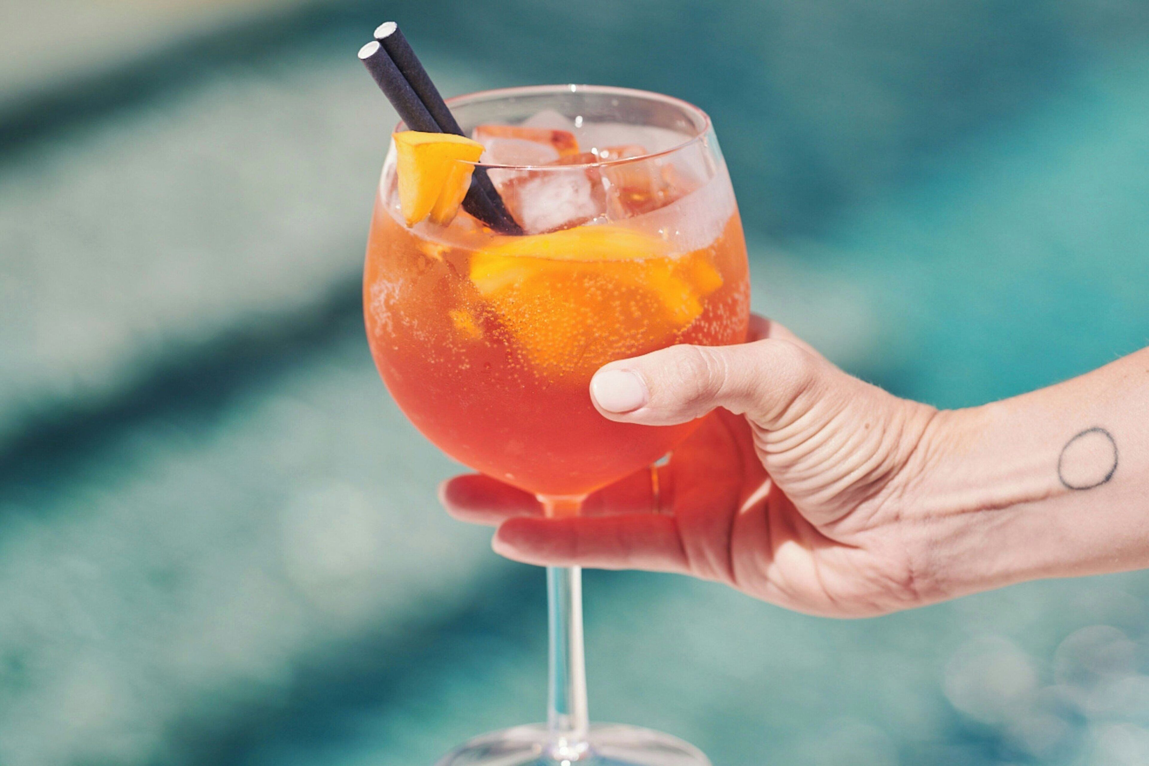 Une main tenant un verre à cocktail rempli de glace et décoré de fruits.