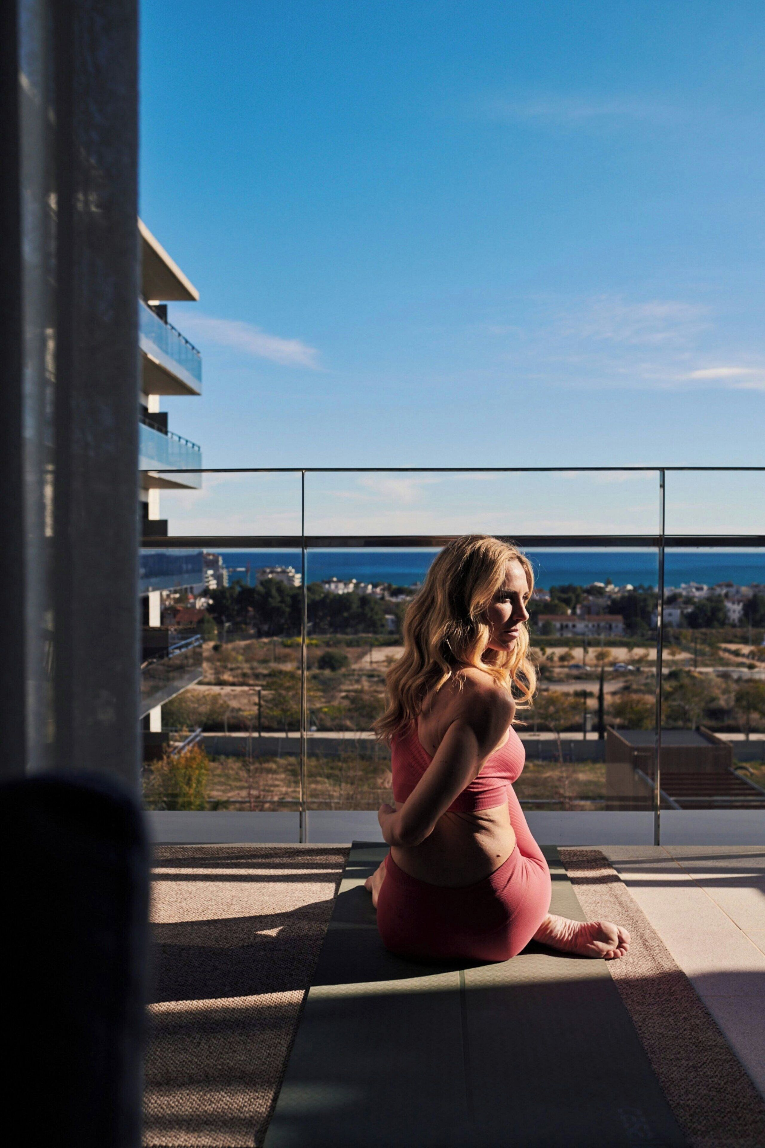 Une personne assise sur un balcon, avec vue sur la mer et les bâtiments.