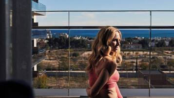 A person sitting on a balcony with a view of the sea and buildings.