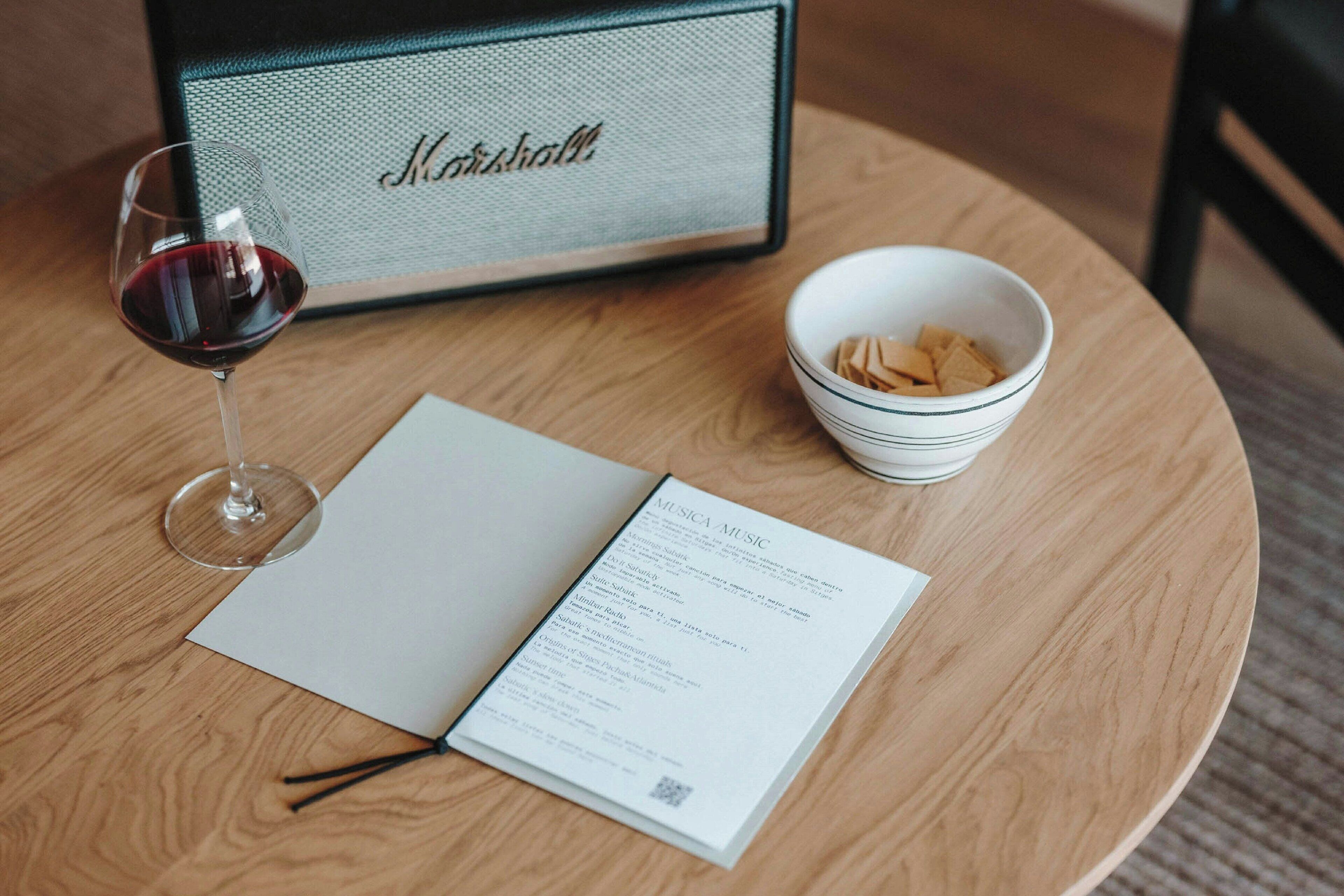 Una mesa con un menú, una copa de vino tinto y un bol de galletas.
