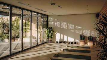 A spacious room with large windows, a yoga mat area, and a plant.