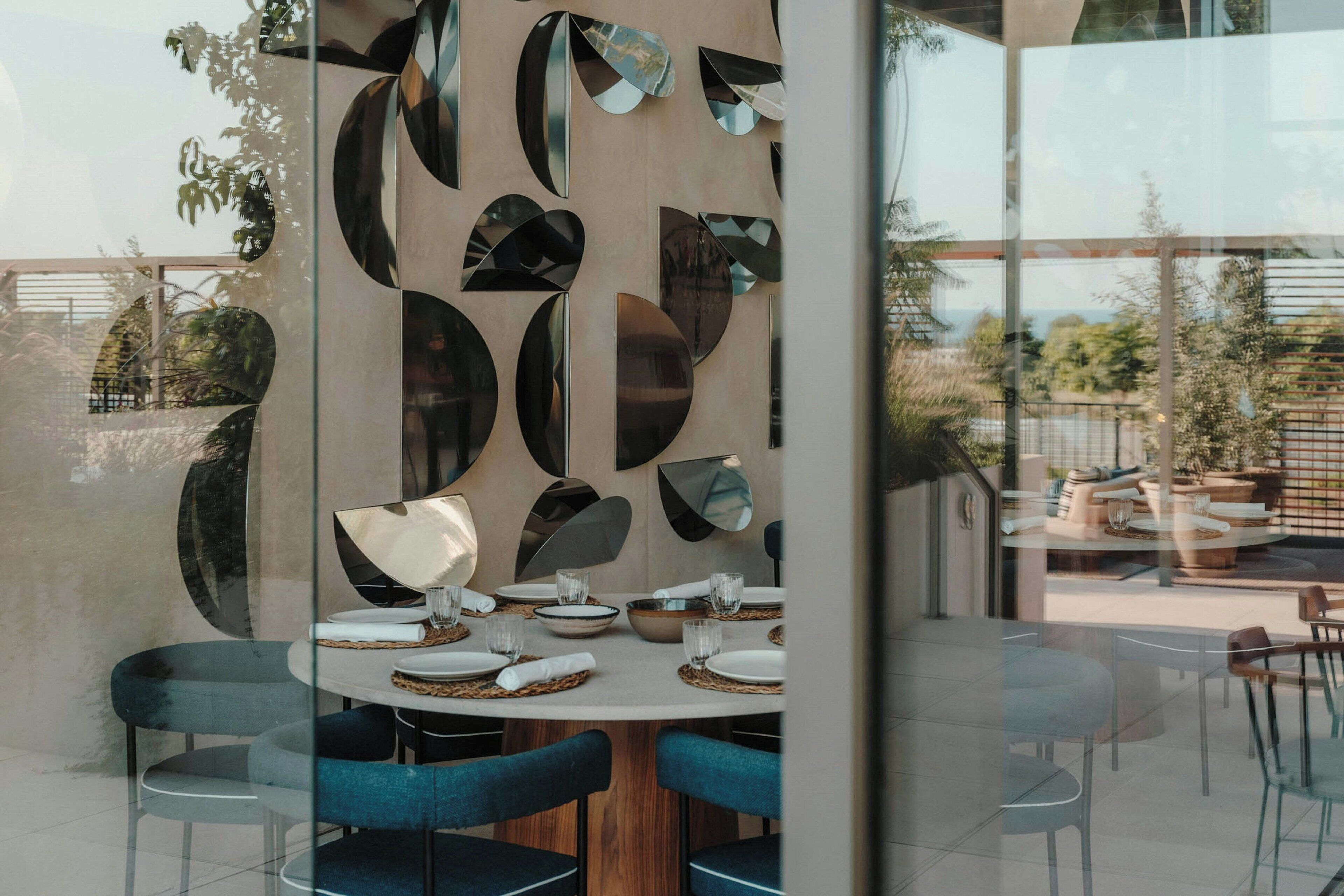 A modern dining area with a round table set for four, surrounded by blue chairs.