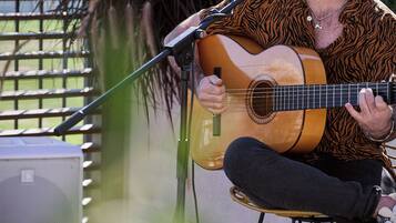Une personne joue de la guitare acoustique assise sur une chaise, à l'extérieur.