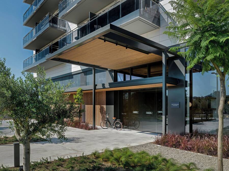 Un edificio moderno con vestíbulo cubierto, barandillas de vidrio y una bicicleta estacionada afuera.