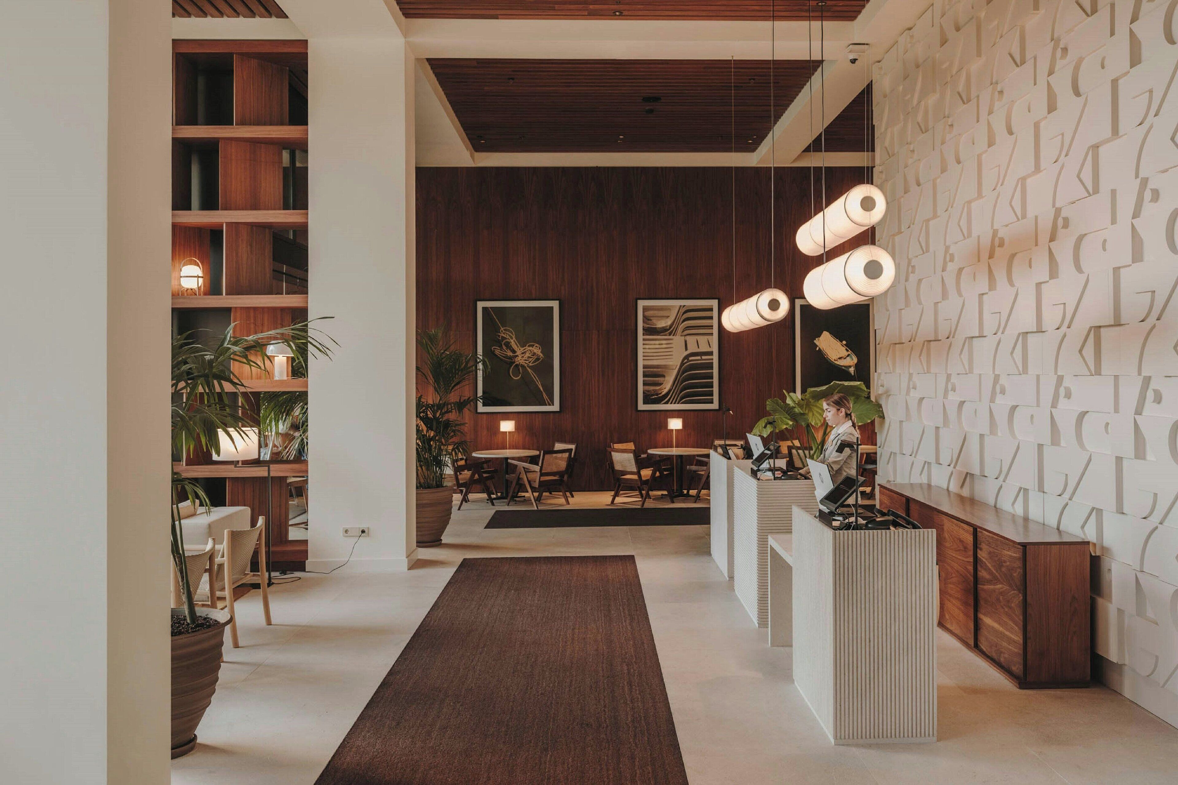Un'accoglienza moderna con una reception in legno, una parete decorata e un’area salotto centrale con tavoli e sedie.