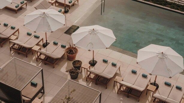 Un área de piscina en la azotea con sillones de descanso y sombrillas.